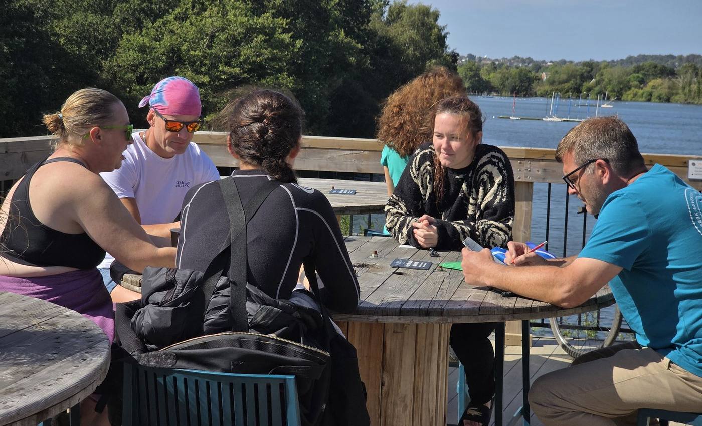 Students round a table by the lake going through dive theory with their instructor