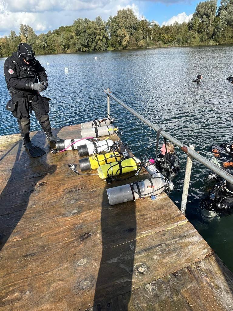 Sidemount cylinders laid out on a lake pontoon with a drysuit diver kitting up