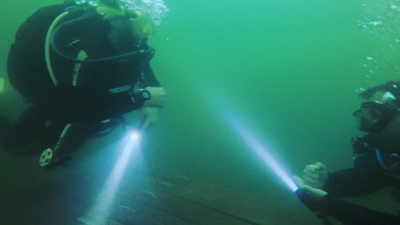 Two divers with torches in green UK lake water