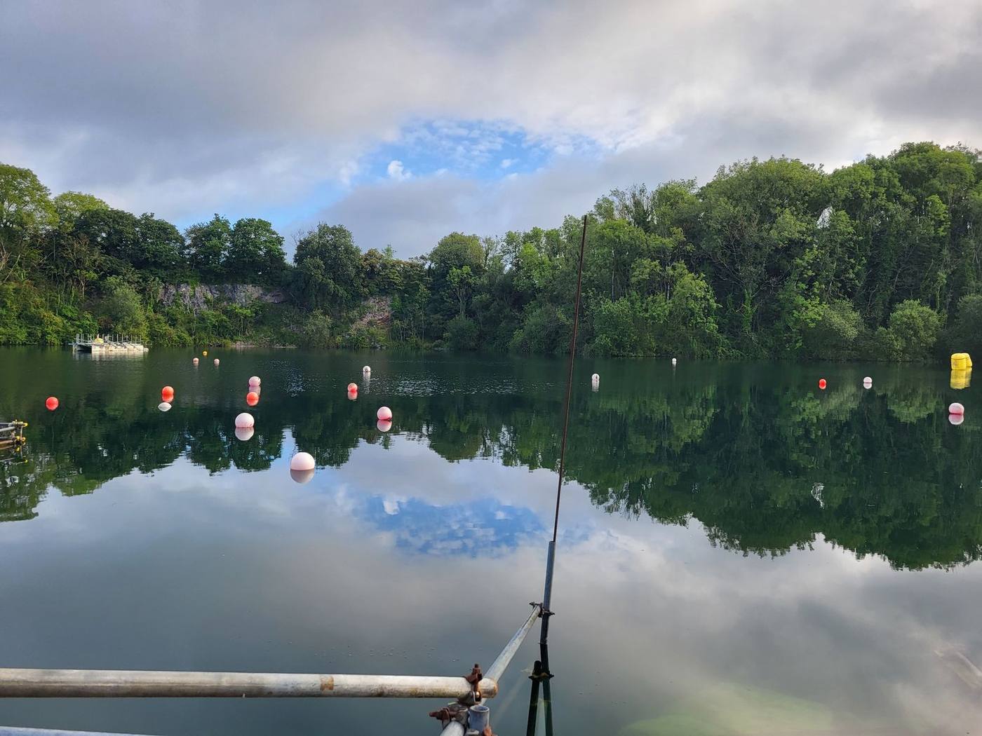 A still summer morning at a UK inland quarry dive site, buoys and trees reflected in the water