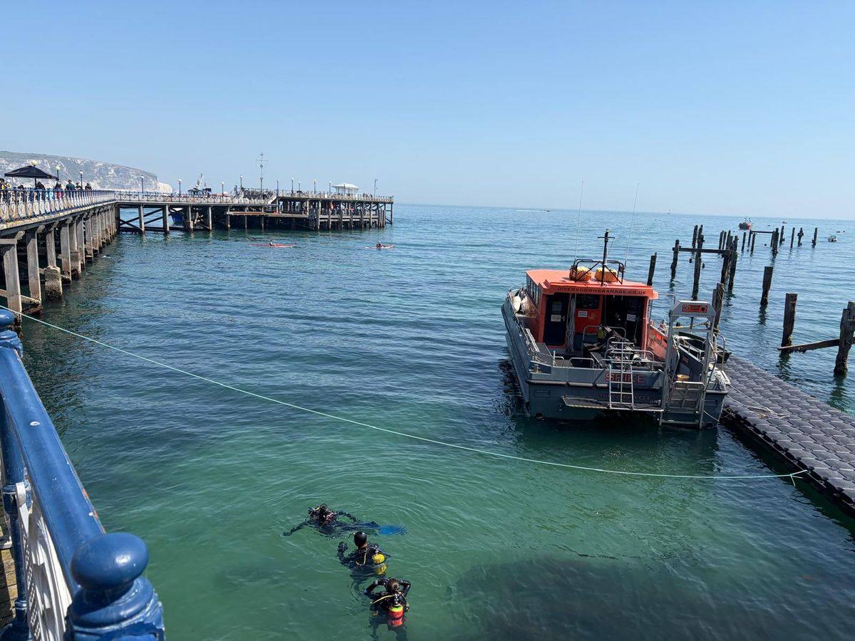 Divers finning out beside Swanage pier with a dive boat moored alongside
